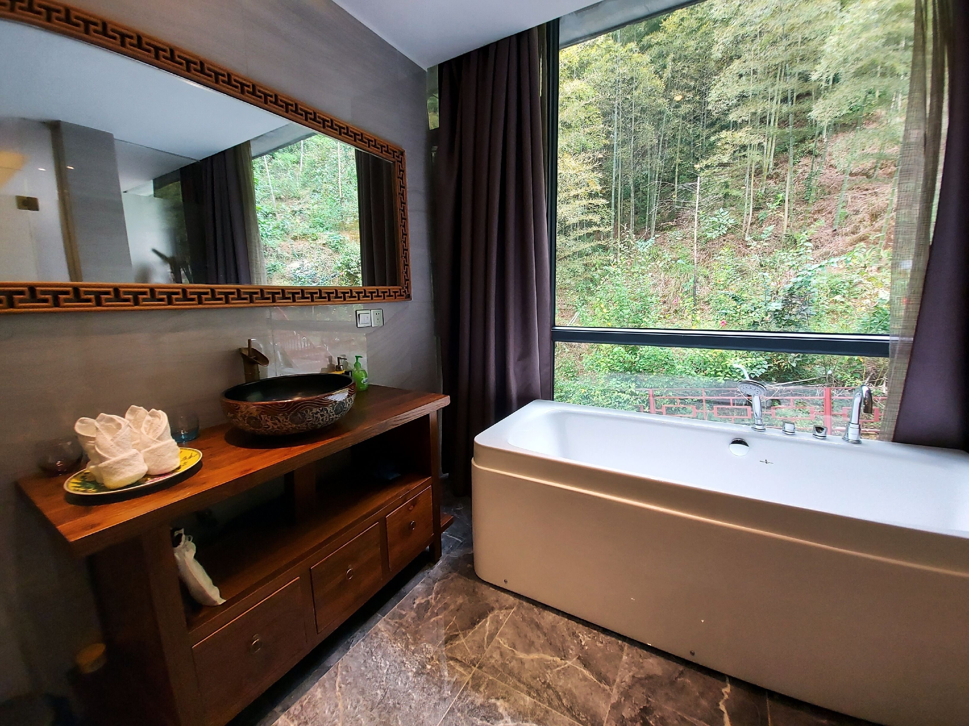 Un baño con un ventanal grande, un tocador de madera, un lavabo sobre encimera y una bañera independiente.