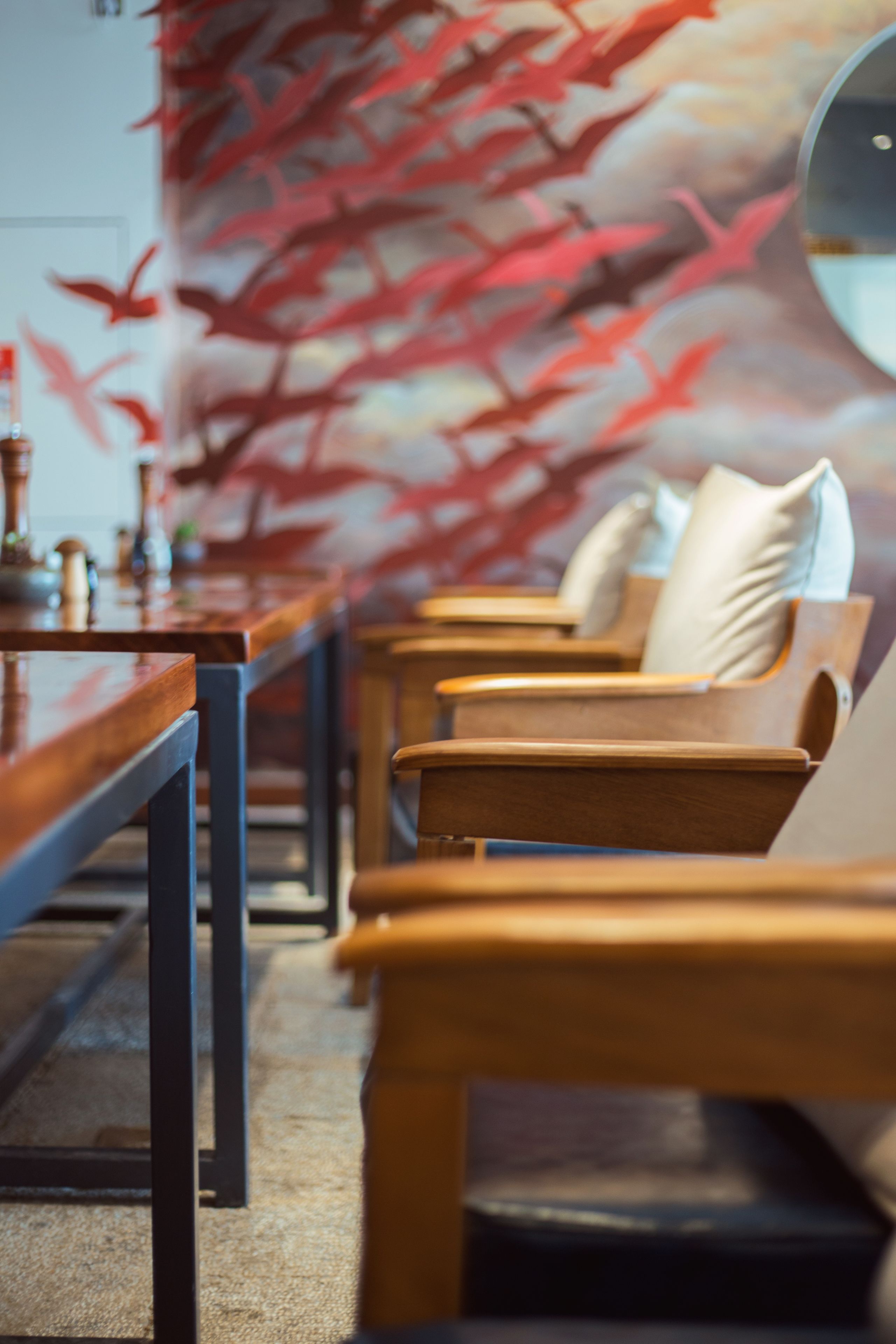 A row of wooden chairs with cushions, a wooden table, and a wall with a red abstract design.