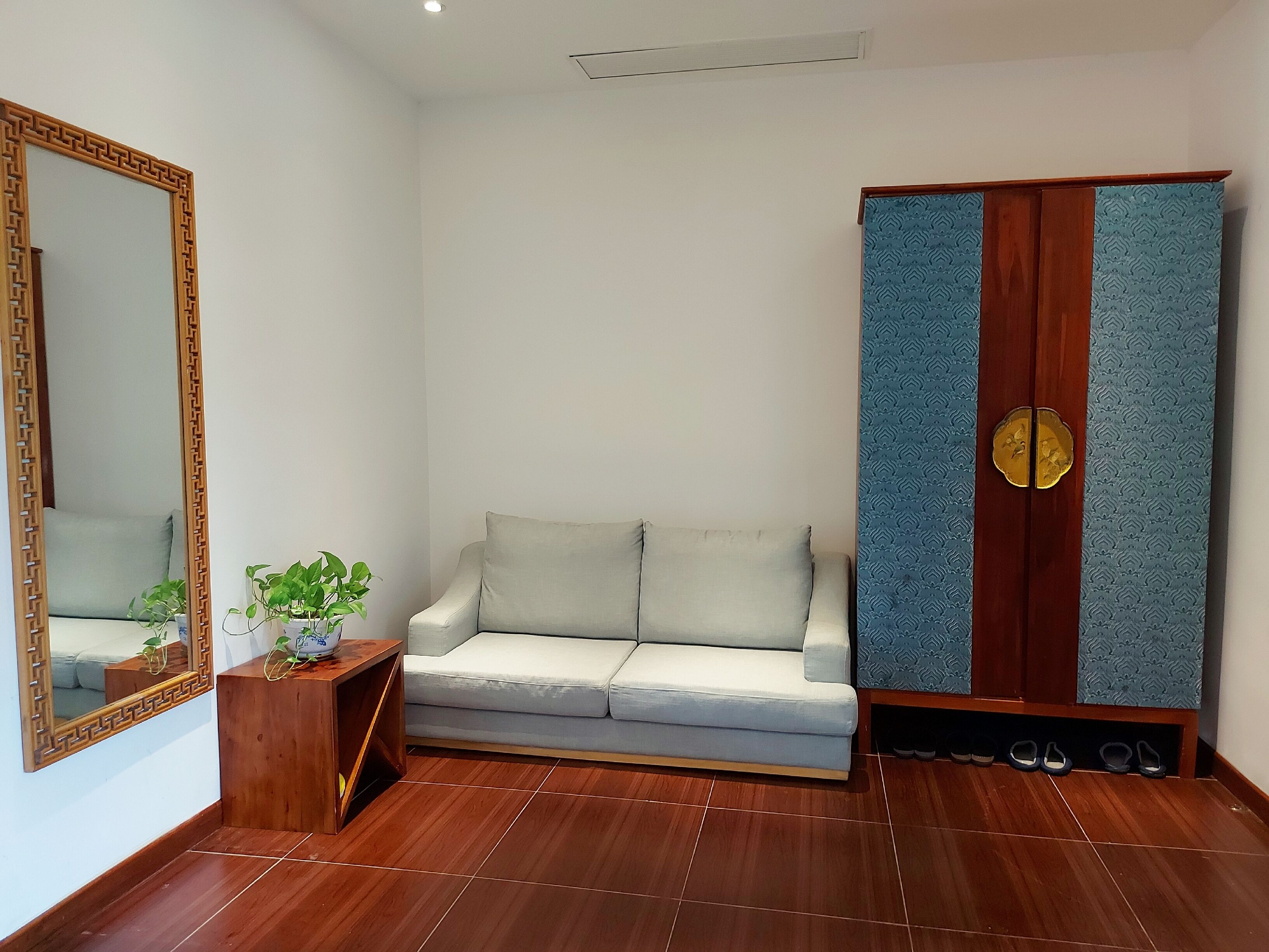 A room with a sofa, a wooden cabinet, a mirror, and a potted plant.