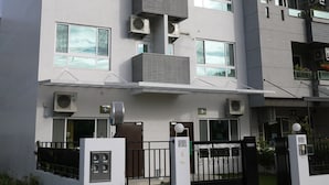 Un edificio moderno de varios pisos con balcones, unidades de aire acondicionado y una entrada con portón.
