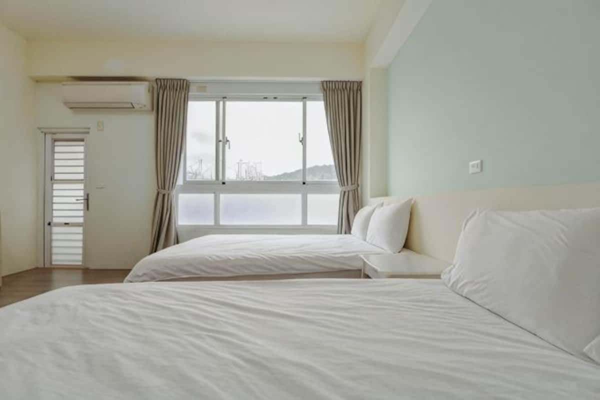 Una habitación con dos camas, una ventana con cortinas, una puerta y un aire acondicionado.