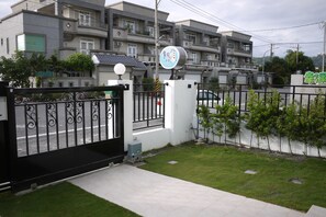 Zona residencial cerrada con un edificio de apartamentos moderno, un letrero con caracteres chinos y un césped bien cuidado.