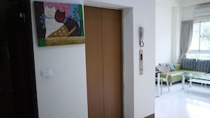 Una habitación con puerta de madera, un cuadro, un teléfono, un sofá y una ventana con cortinas.
