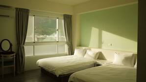 Habitación con dos camas, una silla, una ventana con cortinas y vistas a zonas verdes.
