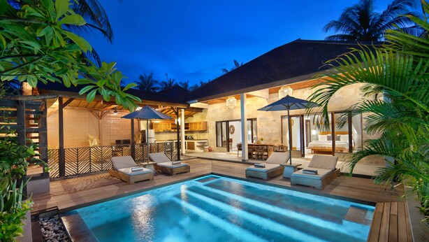A poolside area with lounge chairs and umbrellas, a wooden deck, and a modern building with a kitchen and dining area. - Utara Villas (Gili Trawangan)