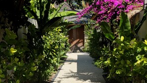 A pathway leading to a building with a wooden door, surrounded by lush greenery and flowering plants. - Utara Villas (Gili Trawangan)