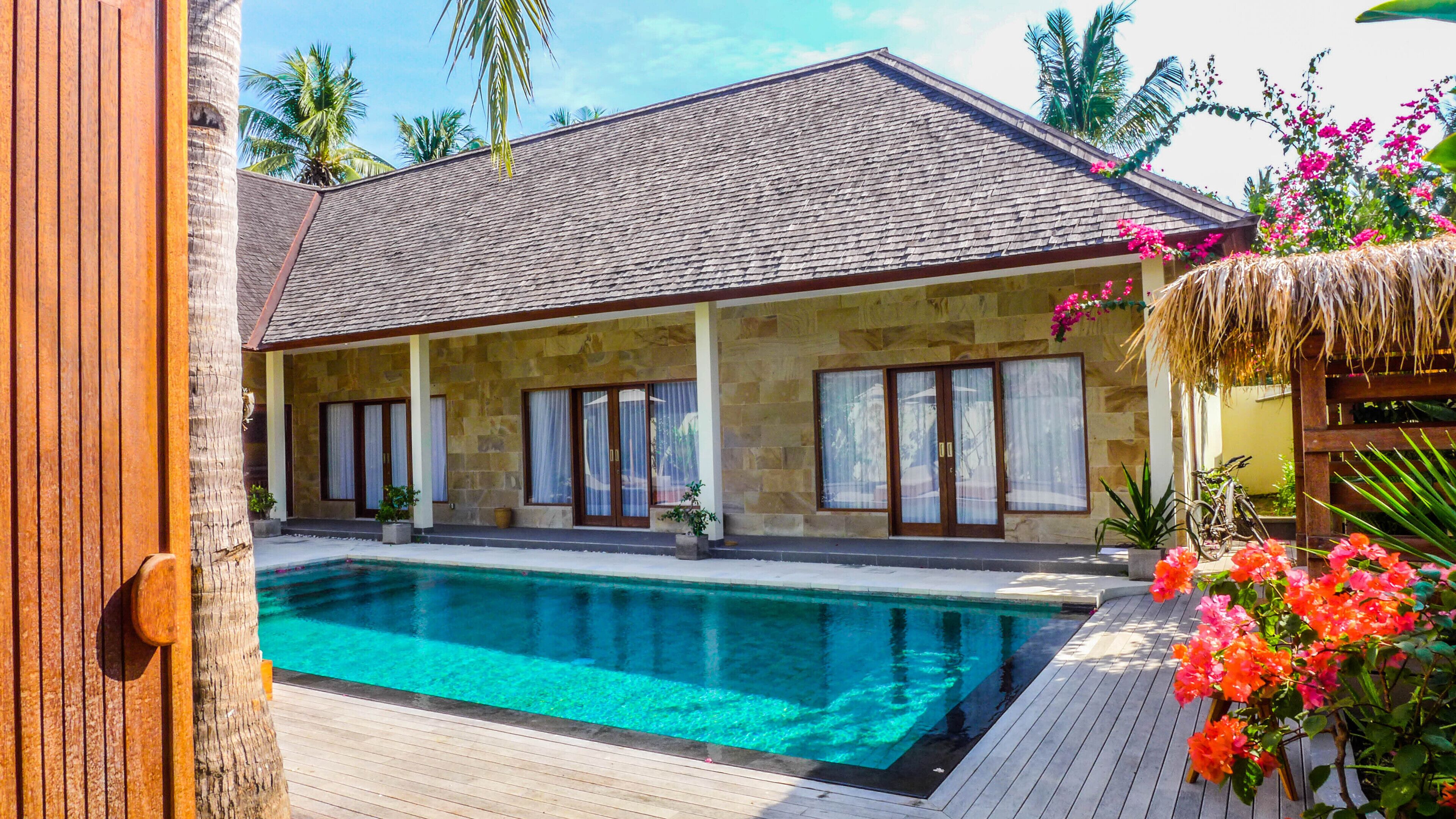 A two-story stone building with a swimming pool, large windows, and tropical plants.