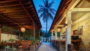 An outdoor bar area with wooden furniture and a view of a palm tree. - Utara Villas (Gili Trawangan)