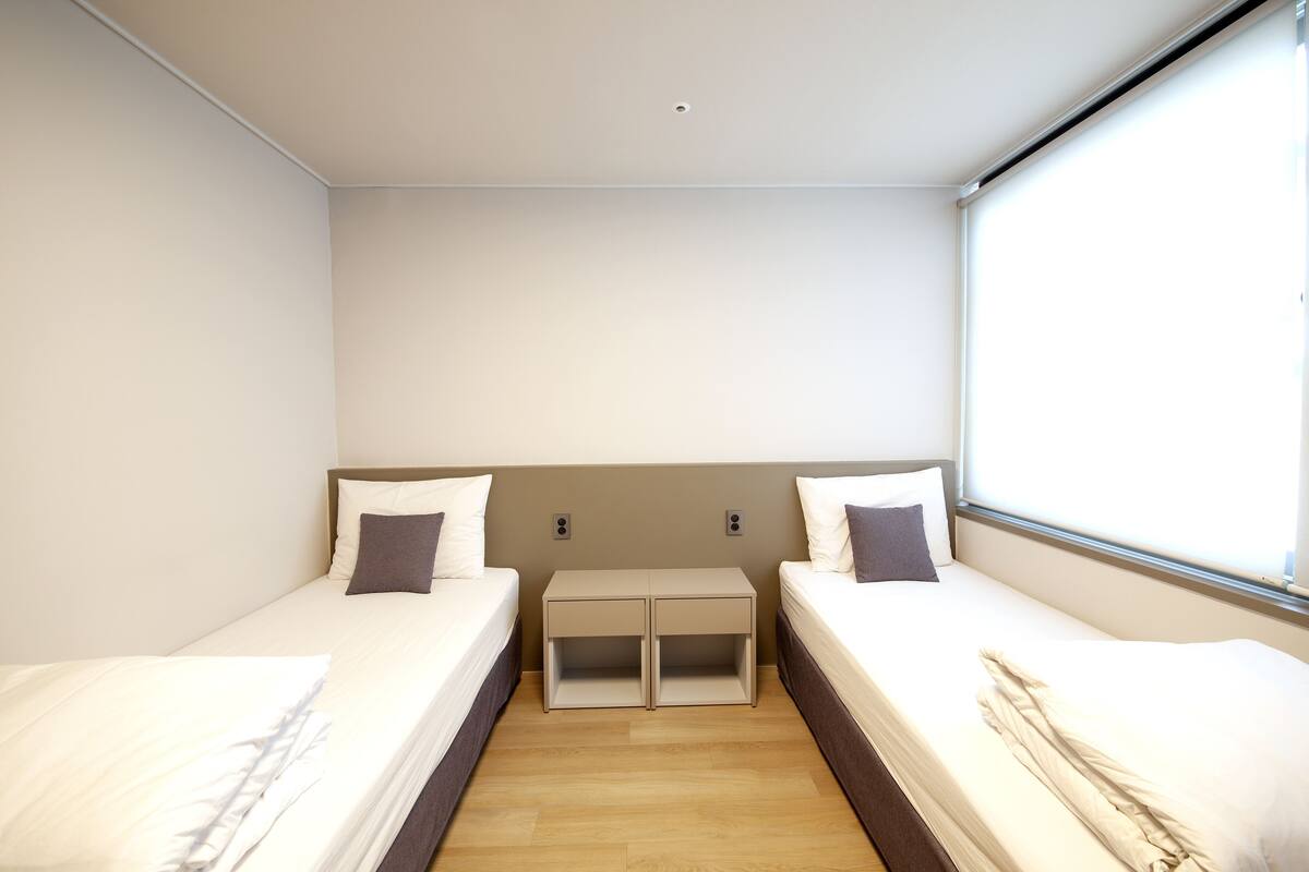 Habitación doble con dos camas, una mesita y una ventana.
