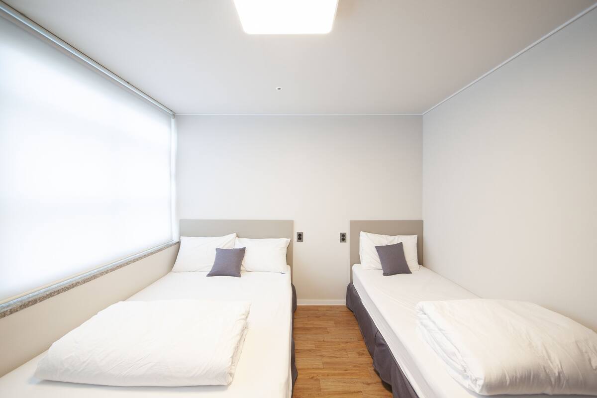 Una habitación pequeña y limpia con dos camas individuales, una ventana y una lámpara en el techo.
