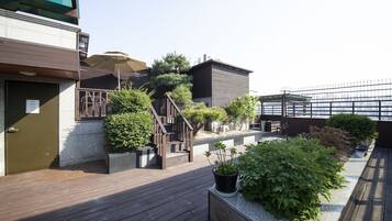 A rooftop garden with wooden decking, potted plants, and a staircase leading to a building entrance.