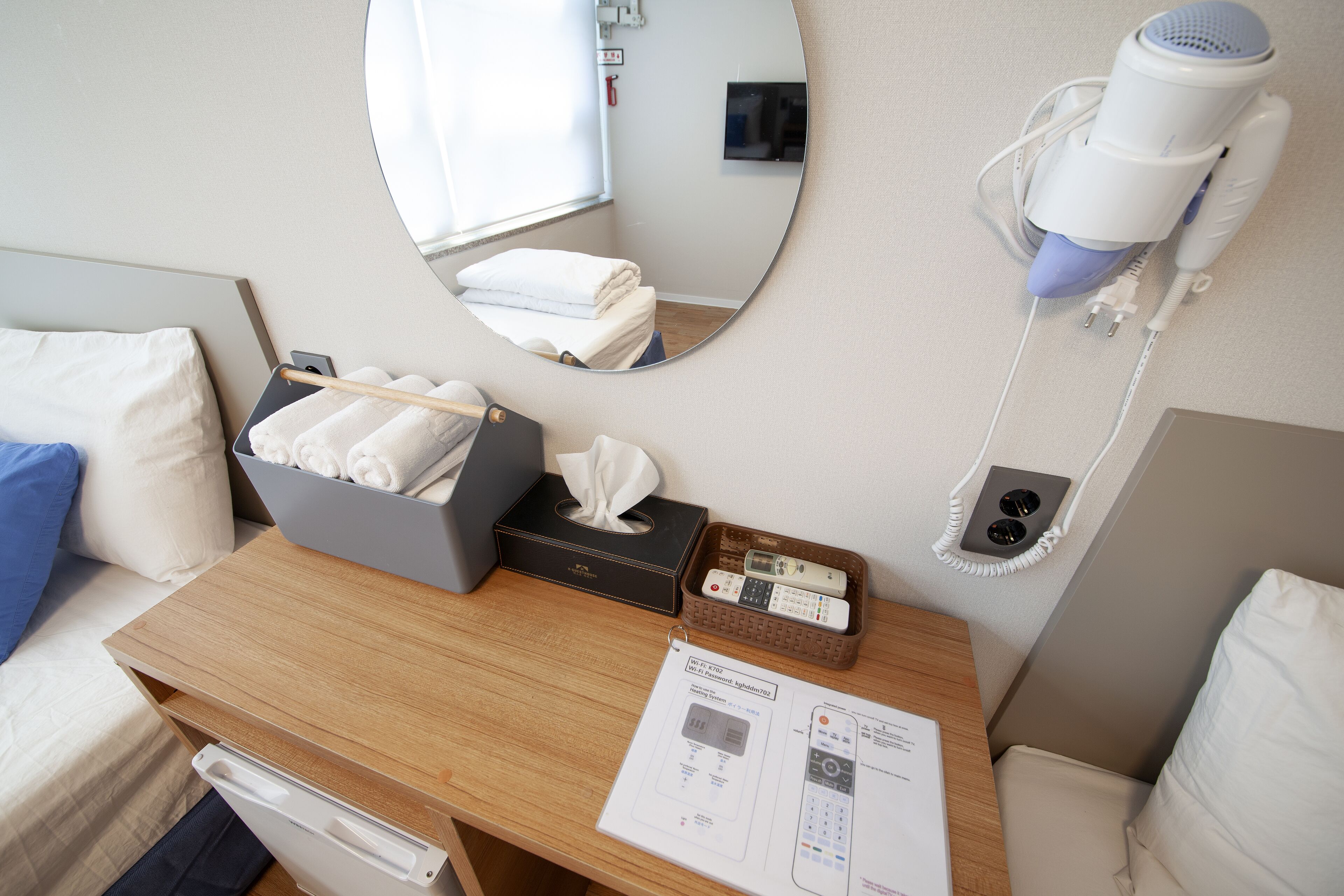 Quarto de hotel com escrivaninha de madeira, espelho, secador de cabelo, controle remoto e caixa de lenços.
