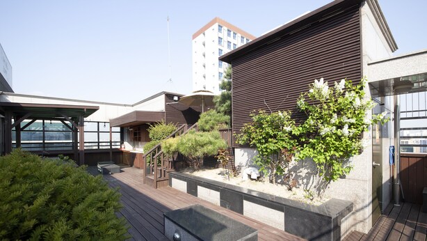 A modern outdoor deck with a wooden floor, a black rectangular planter, and a small tree. - K- Grand Hostel Dongdaemun (Seoul)