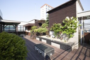 A modern outdoor deck with a wooden floor, a black rectangular planter, and a small tree. - K- Grand Hostel Dongdaemun (Seoul)