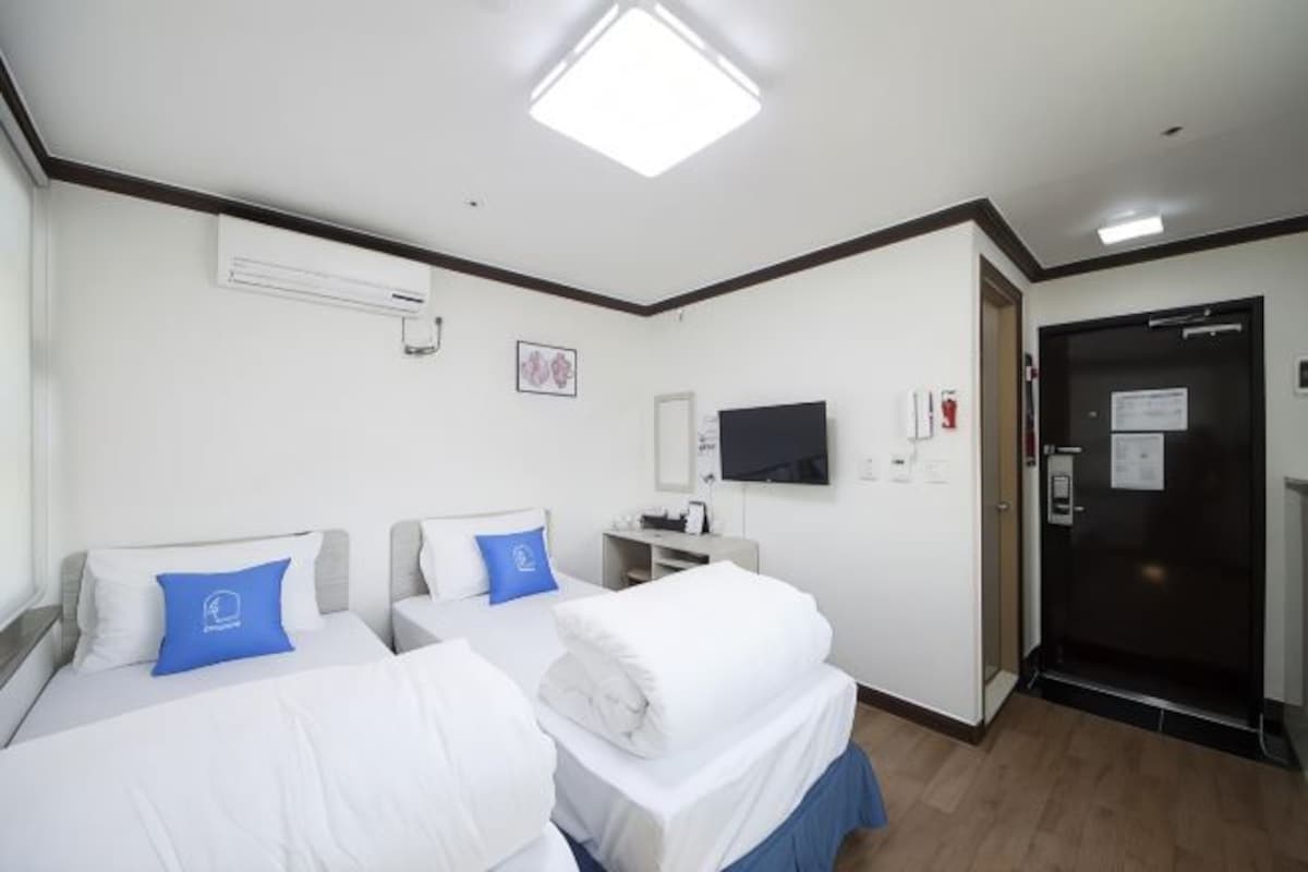 A hotel room with two beds, a flat-screen TV, an air conditioning unit, and a door with a sign.
