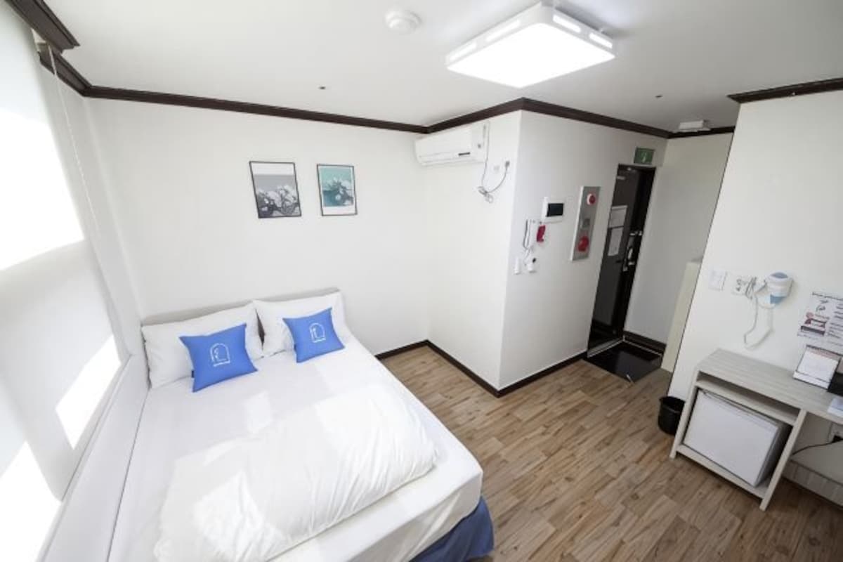 A hotel room with a bed, a desk, a chair, a window, and a door.