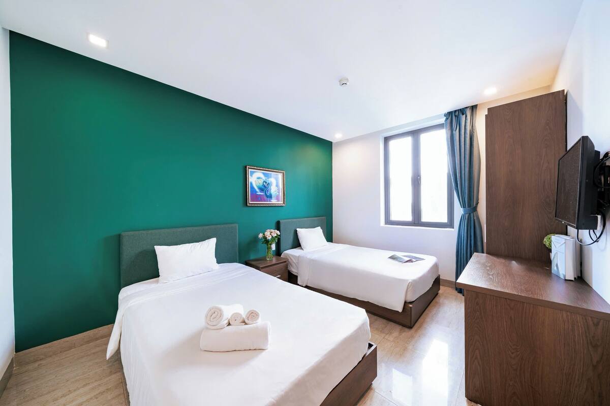Une chambre d’hôtel avec deux lits, un bureau en bois, une télévision et une fenêtre avec des rideaux.