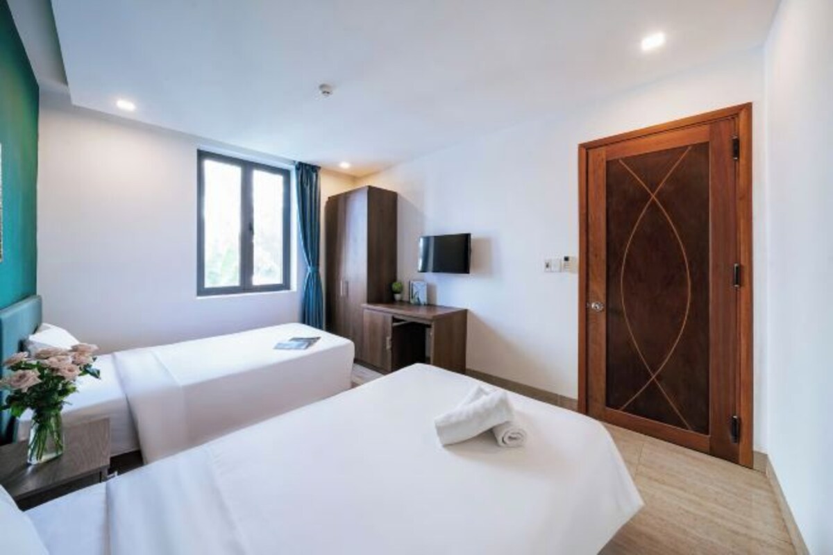 A hotel room with two beds, a desk, a TV, and a wooden door.