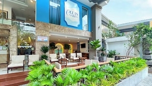 Entrada de un hotel con un letrero azul que dice "Ocean Garden", mesas al aire libre con plantas y un cartel que indica "Ocean Glow".