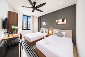 Une chambre d’hôtel avec deux lits, un bureau, un ventilateur de plafond et des œuvres d’art accrochées aux murs.