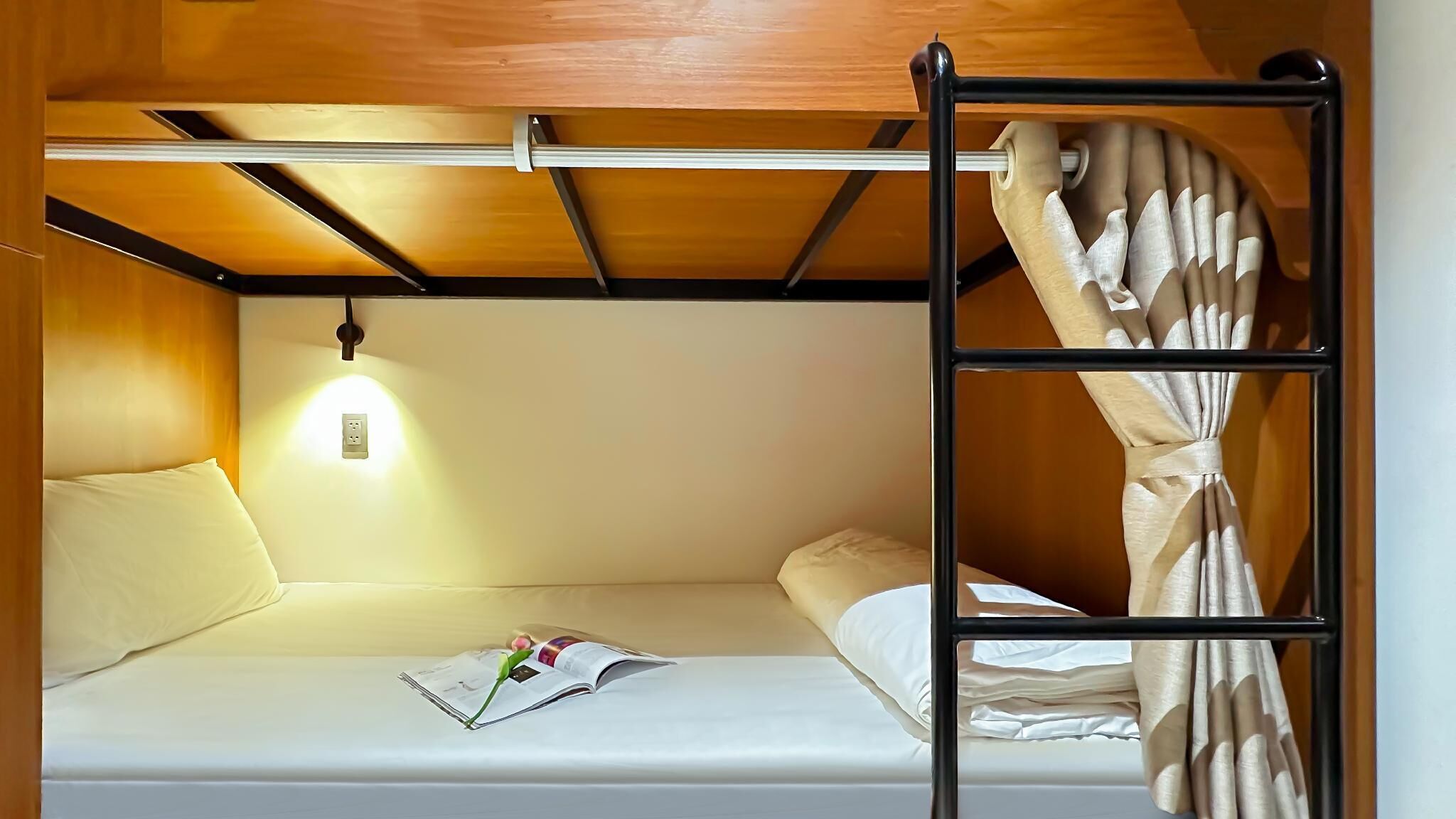 A bunk bed with a headboard, a bedside lamp, and a book on the lower bunk.