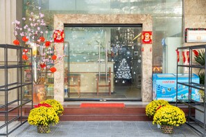 A hotel entrance with a glass door, a Christmas tree, and two potted yellow flowers. - Ocean Garden Boutique Da Nang a Salve by Haviland (Da Nang)