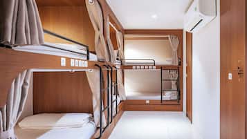Quarto compacto e bem iluminado, com beliches, paredes de madeira e um guarda-roupa pequeno.