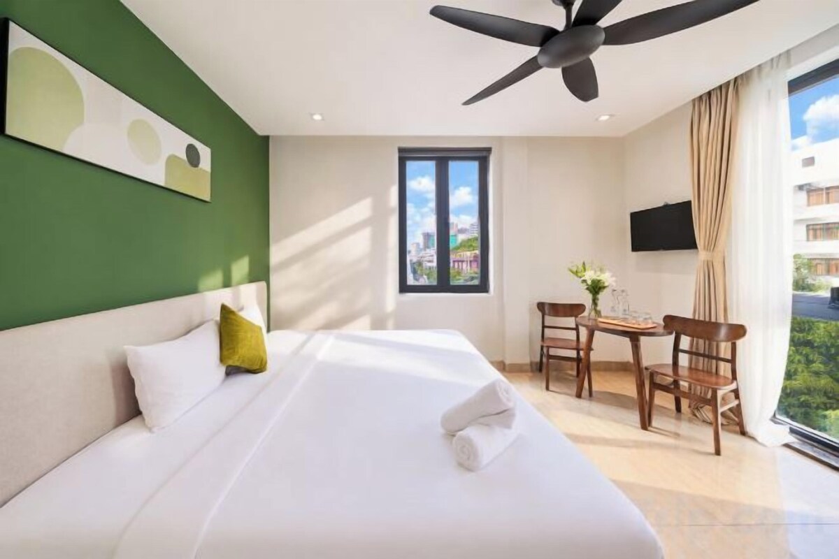Een hotelkamer met een bed, een plafondventilator, een raam, een bureau en een stoel.