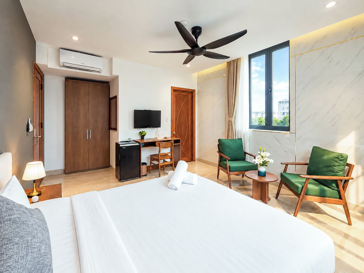 A hotel room with a bed, desk, chairs, a television, and a ceiling fan.