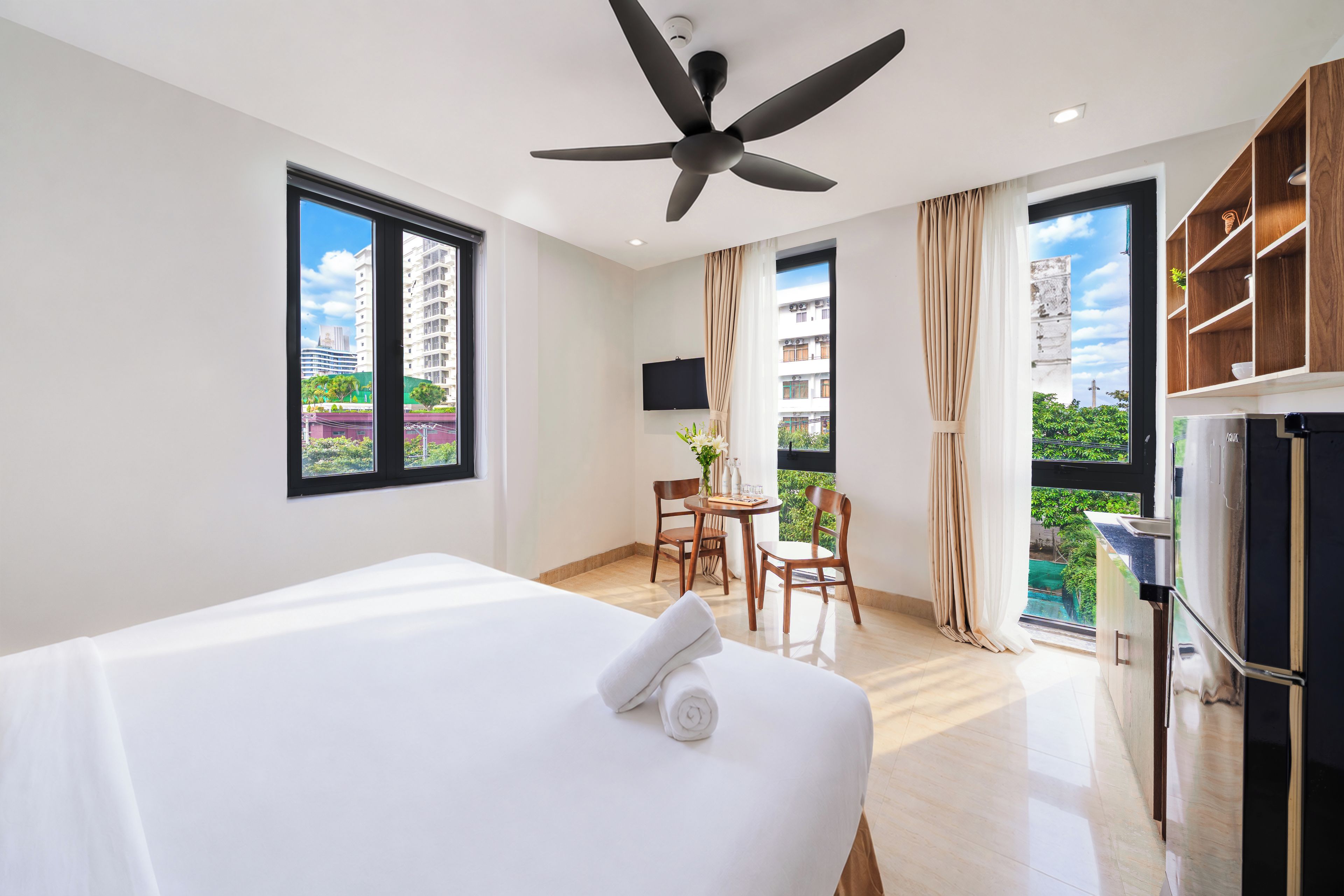 A hotel room with a bed, a desk, a chair, a ceiling fan, and a TV.