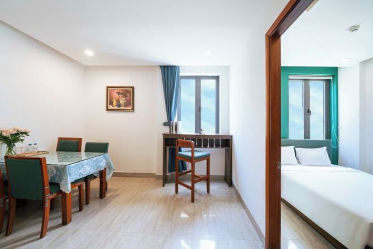 Een hotelkamer met een bed, een bureau met stoel, een eettafel met stoelen, en een raam met gordijnen.