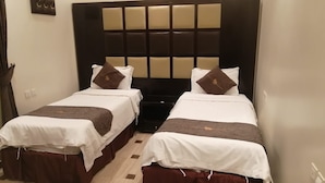 Une chambre d’hôtel avec deux lits simples, une grande tête de lit rembourrée et une petite table de chevet.