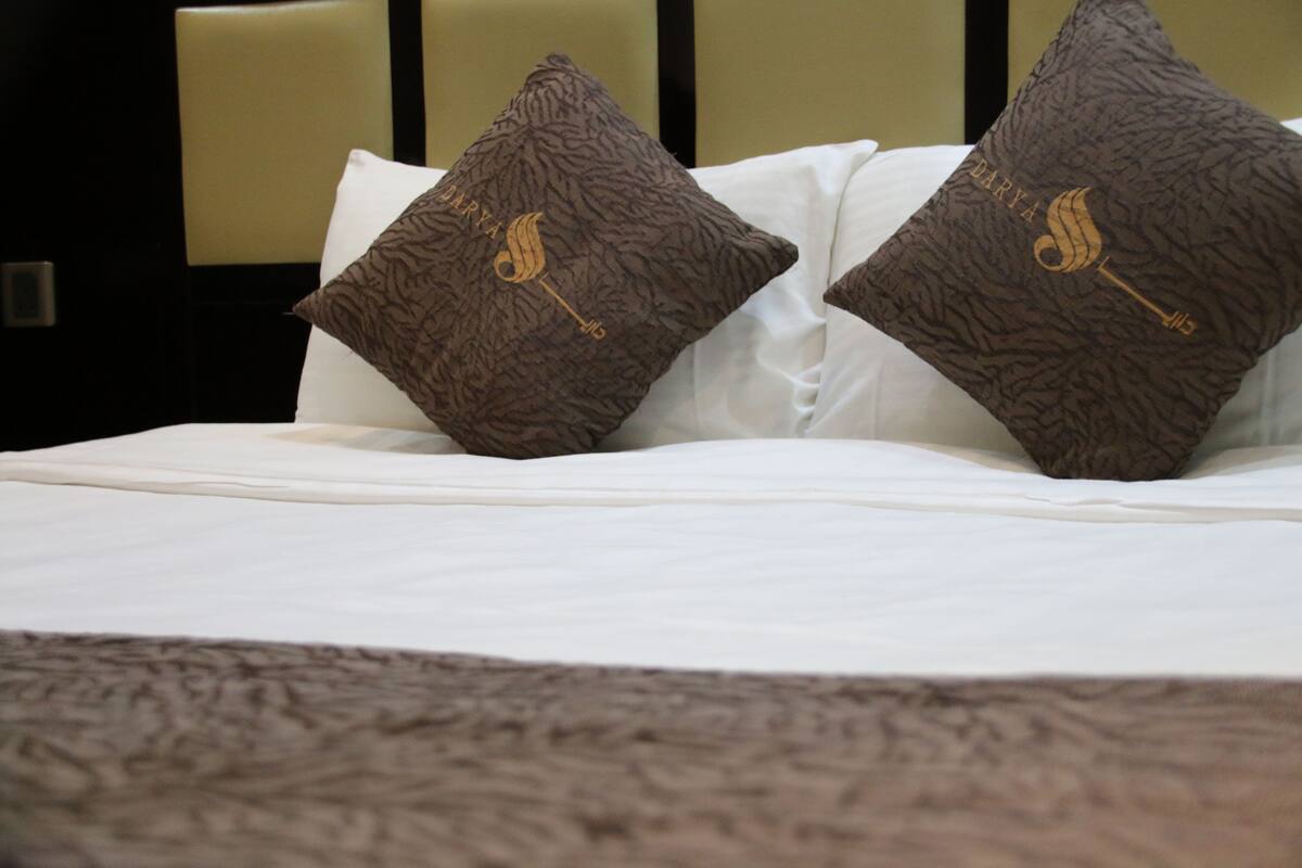 Ein Bett mit weißen Leinen und zwei braunen Kissen mit Goldstickerei.
