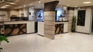 Un hall d’hôtel moderne avec un comptoir d’accueil, une grande plante en pot et un sol carrelé, propre et bien entretenu.