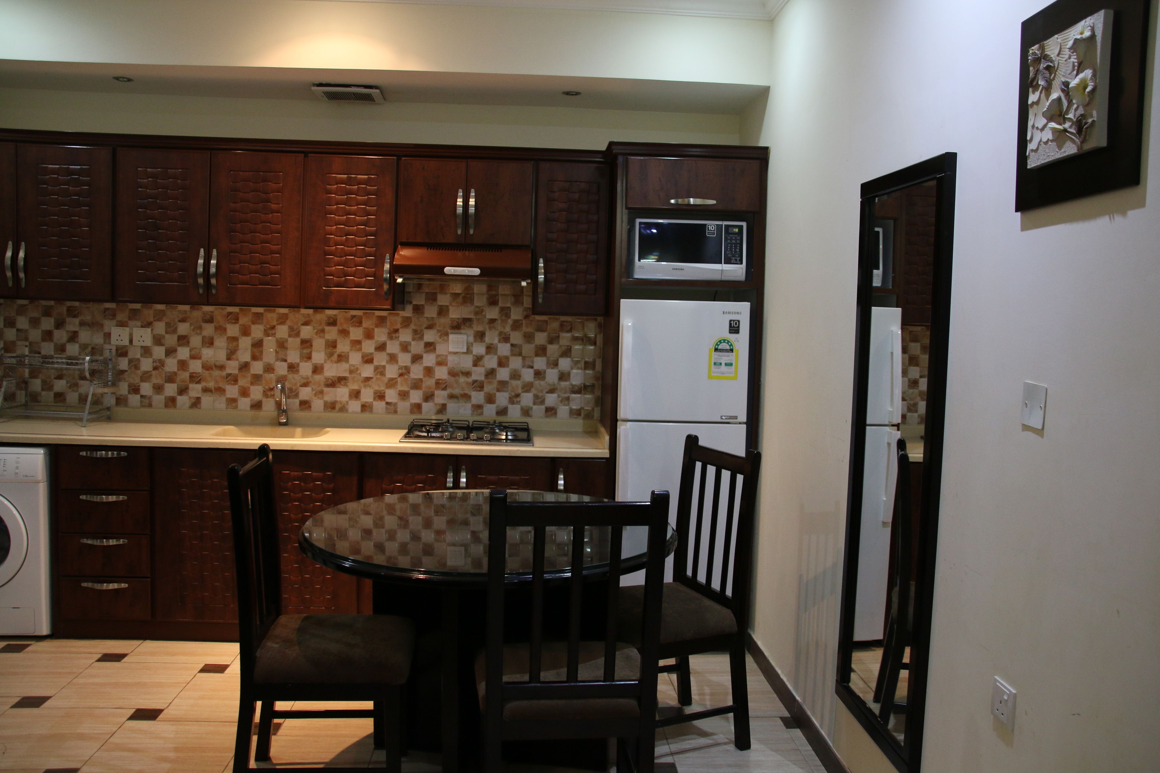 A compact kitchen with wooden cabinets, a microwave, a refrigerator, and a dining table with chairs.