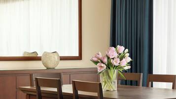Une table à manger ornée d’un vase de fleurs, des chaises en bois et une fenêtre avec des rideaux.