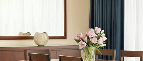 A dining table with a vase of flowers, wooden chairs, and a window with curtains.