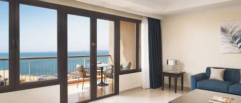 A spacious living room with a balcony overlooking a beach, a sofa, a coffee table, and a painting on the wall.