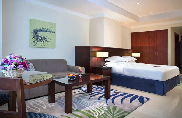 A hotel room with a bed, a sofa, a coffee table, a side table, and a wall-mounted lamp. - Sedra Arjaan By Rotana (Doha)