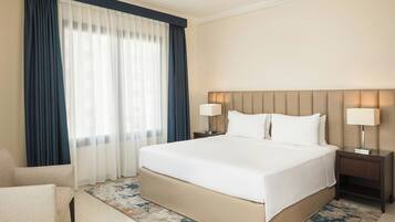 Habitación de hotel con una cama grande, dos mesitas de noche con lámparas, una silla y un ventanal con cortinas.