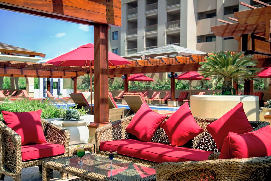 A poolside area with wicker furniture, red cushions, and umbrellas.