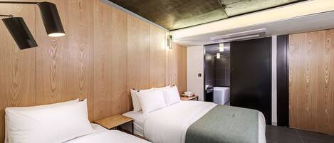 A hotel room with two beds, wooden panel walls, a concrete ceiling, and a modern design.