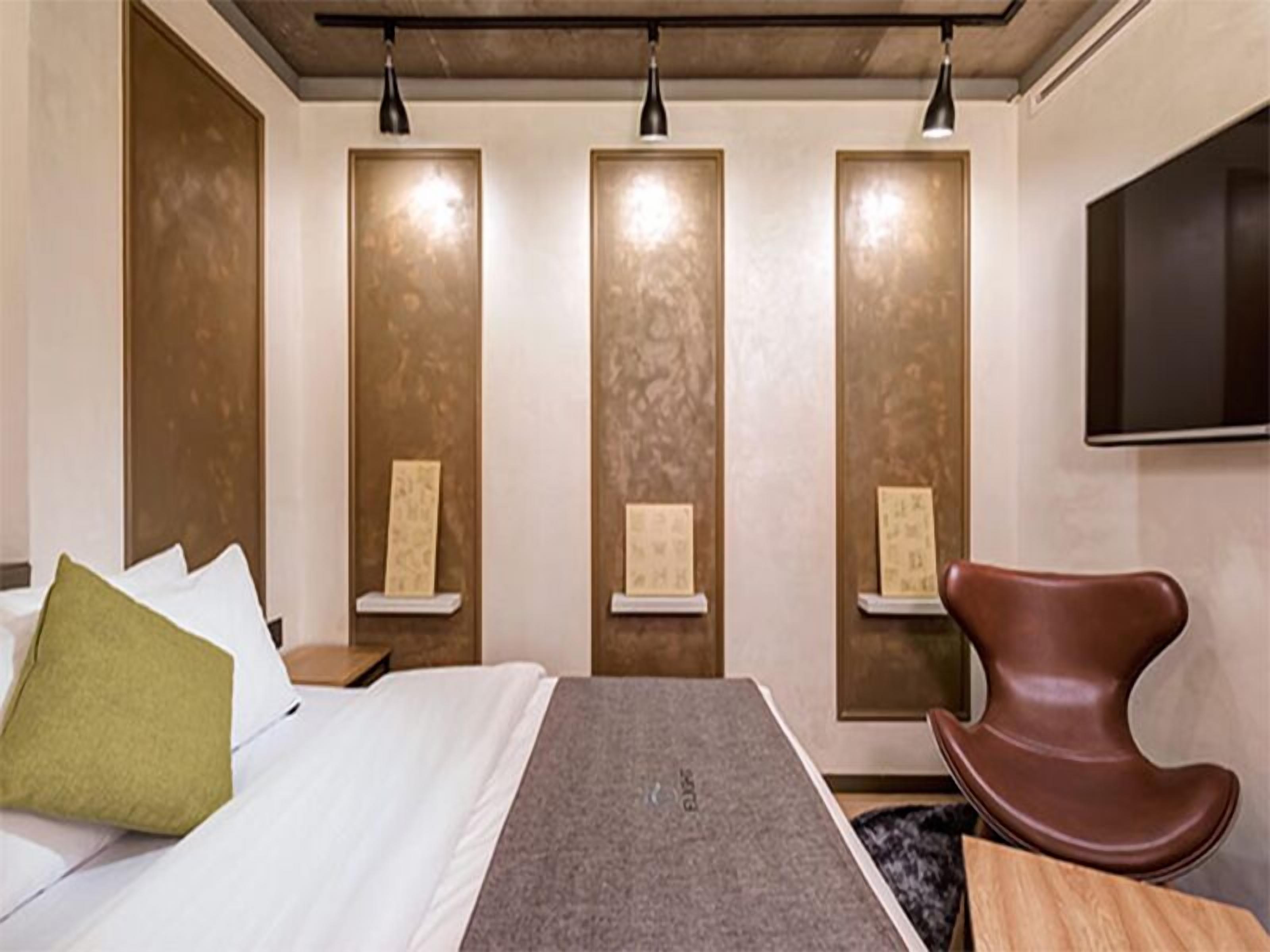Ein Hotelzimmer mit einem Bett, einem braunen Stuhl und drei beleuchteten Vertikalpaneelen.