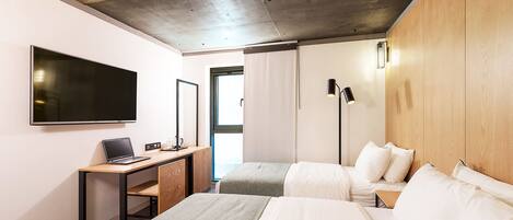 A modern hotel room with a large bed, a desk with a laptop, a flat-screen TV, and a wooden headboard.