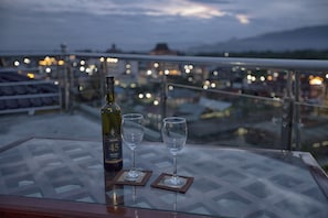 A glass table with a bottle and two wine glasses on a balcony overlooking a cityscape at dusk. - The Hotel Emperor Inle (Nyaungshwe)