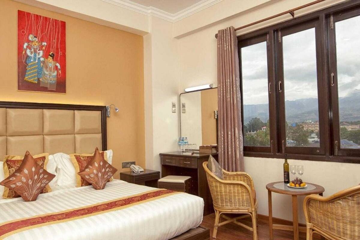 Ein Hotelzimmer mit einem großen Bett, einem Schreibtisch, einem Stuhl und Blick auf die Stadt durch das Fenster.