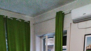 Une pièce avec un canapé rouge, un lit recouvert d’une couette à carreaux verts et blancs, un bureau avec une télévision et des rideaux verts.