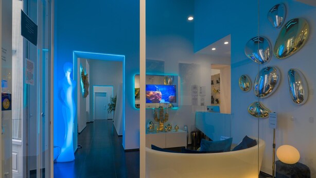 Una hall d'hotel moderna con una reception illuminata di blu, un'area salotto e un divisorio in vetro.