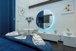 Une chambre d’hôtel moderne avec un grand lit, un miroir rond, une petite table ornée d’un vase de fleurs et un bureau avec une machine à café.