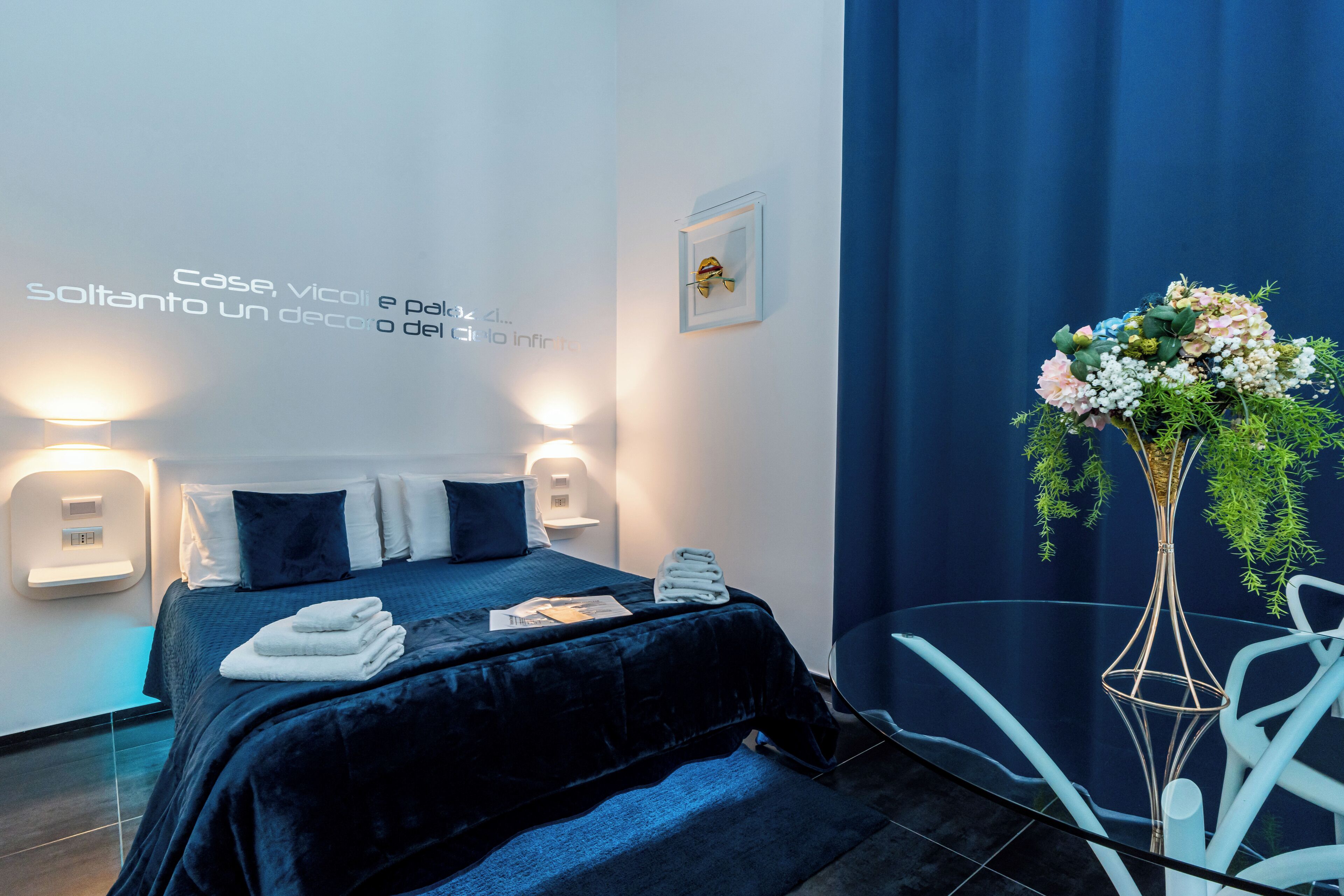 Een moderne hotelkamer met een bed, nachtlampjes, een aan de muur bevestigd kunstwerk en een decoratieve vaas.